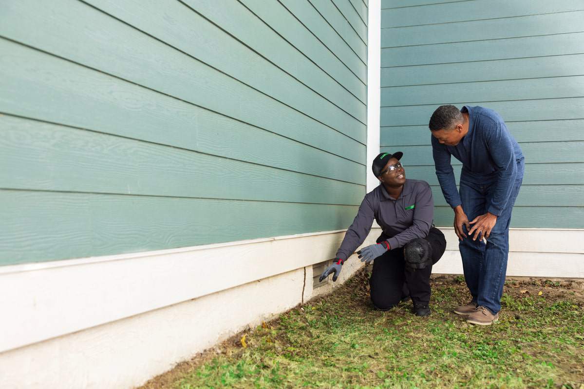 Technician inspecting house foundation for termite damage